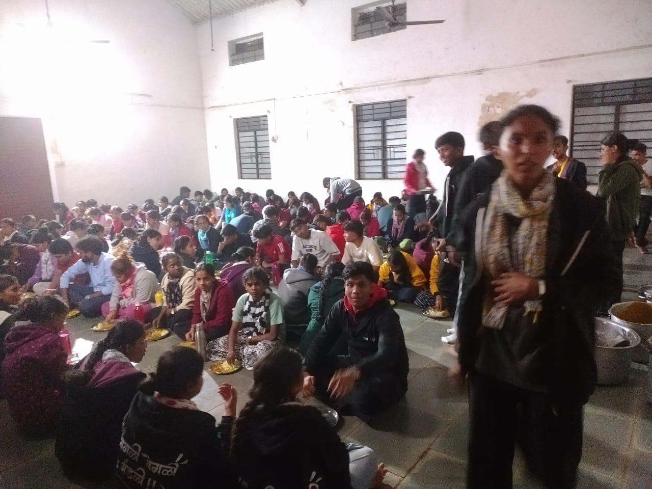 Students seated on the floor of a hall eating a served meal at the NSS camp