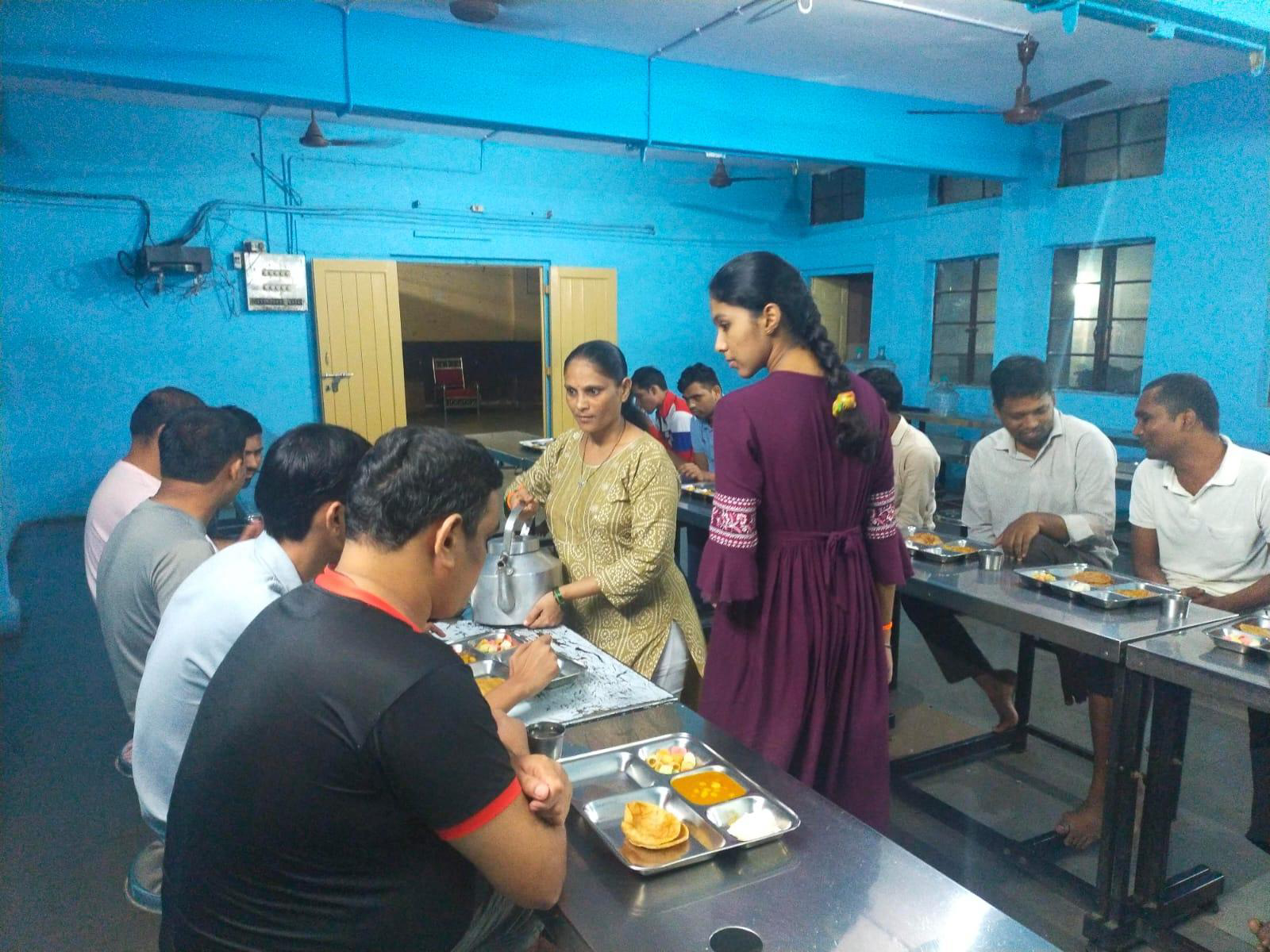 Mayuri and Renuka serving a hot meal of puri, sabzi and sweets to a seated hall of diners